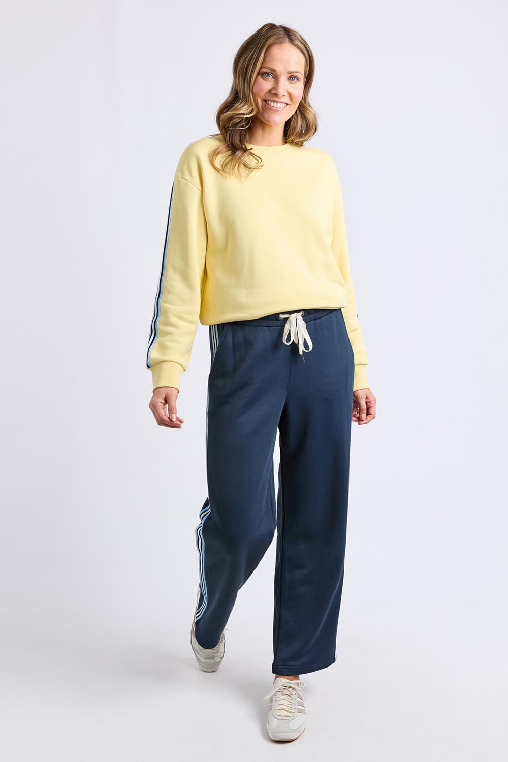 A model wearing the Fundamental Amara Trackpant in colour Navystripe (Blue), from the front, showing the whole outfit