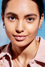 A model wearing the Night Sky Beaded Hoop Earring in colour Bluegold (Blue), from the front, cropped image