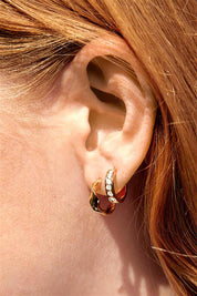A model wearing the Twist Hoop Earring in colour Gold (Metallics), from the front, cropped image