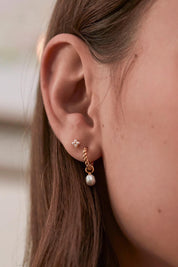 A model wearing the Pearl Drop And Twist Hoop Earrings in colour Goldpearl (Metallics), from the front, cropped image