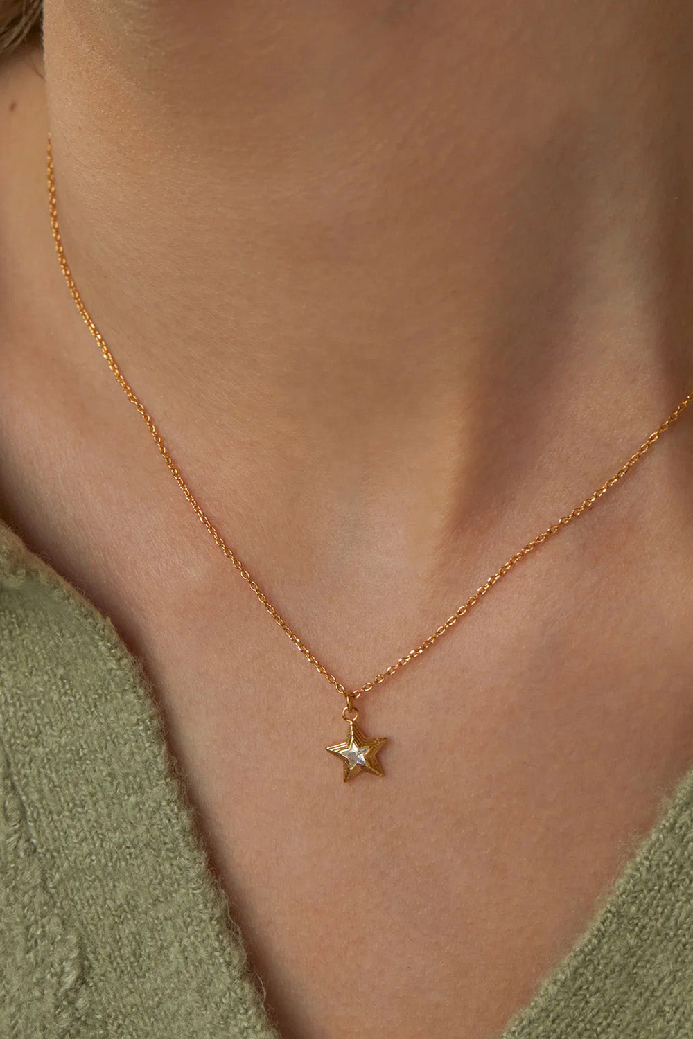A model wearing the Blue Star Necklace in colour Gold (Metallics), from the front, cropped image