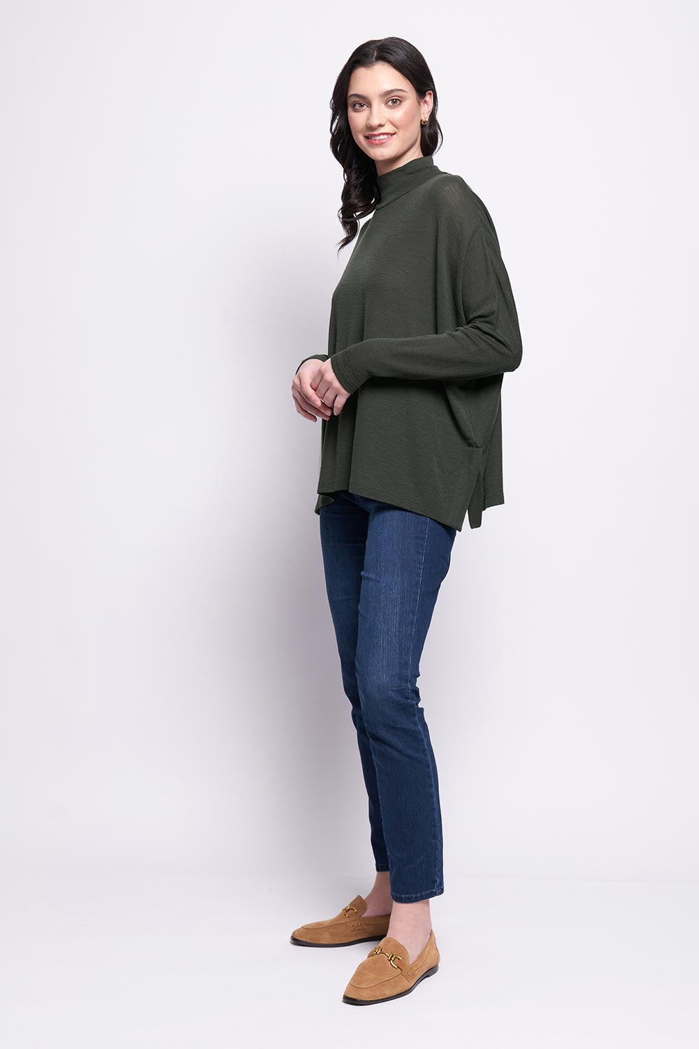 A model wearing the Merino Raisin The Baa Sweater in colour Moss (Green), from the front, showing the whole outfit