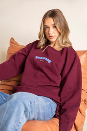 A model wearing the Solace Crew in colour Windwine (Red), from the front, showing the whole outfit