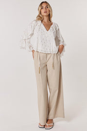 A model wearing the Delia Ruffle Top in colour White (White), from the front, showing the whole outfit