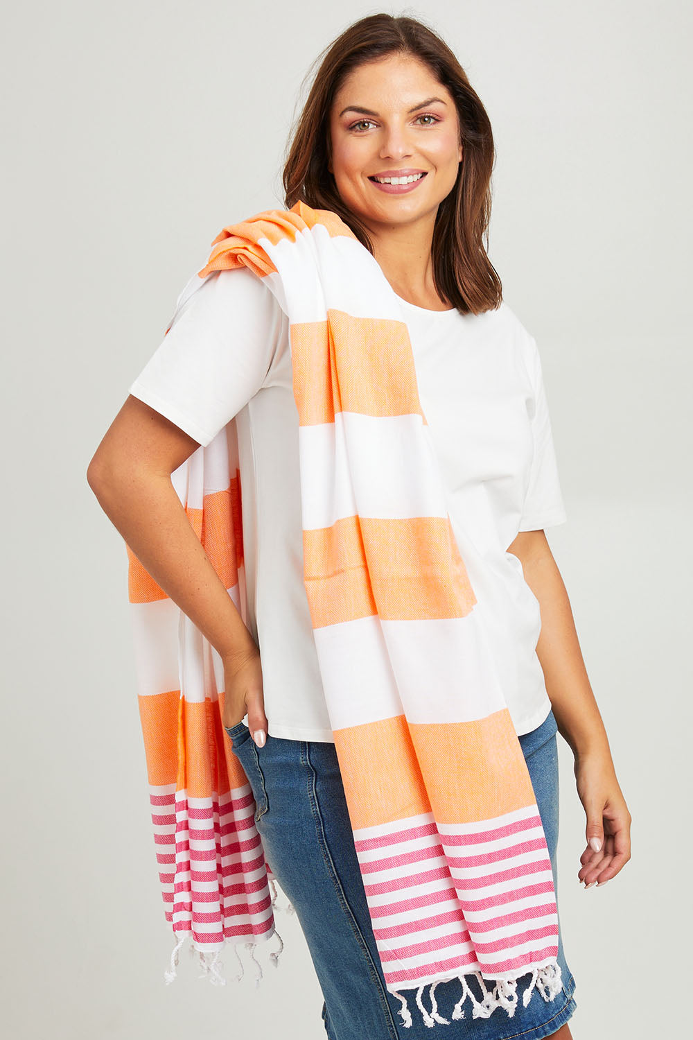 Model Monique wearing the Hammamas Reef Cotton Towel in colour FuschOran, from the front, cropped image