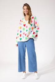 A model wearing the Alaska Relaxed Heart Jumper in colour Rainbow, from the front, showing the whole outfit
