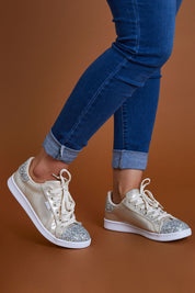 A model wearing size 9 of the Stardust Sneaker in colour Champagne, from the front, cropped image