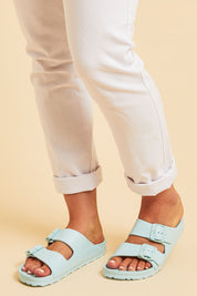 A model wearing size 7 of the Sundreamer EVA Slide in colour Aqua (Blue), from the front, cropped image