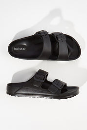 A model wearing size 6 of the Sundreamer EVA Slide in colour Black (Black), from the front, showing the whole outfit