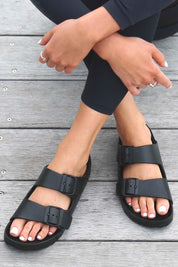 A model wearing the Sundreamer EVA Slide in colour Black (Black), from the front, showing the whole outfit