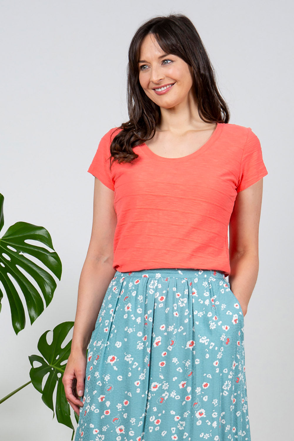 A model wearing the Cockles Tee in colour Papaya (Pink), from the front, cropped image