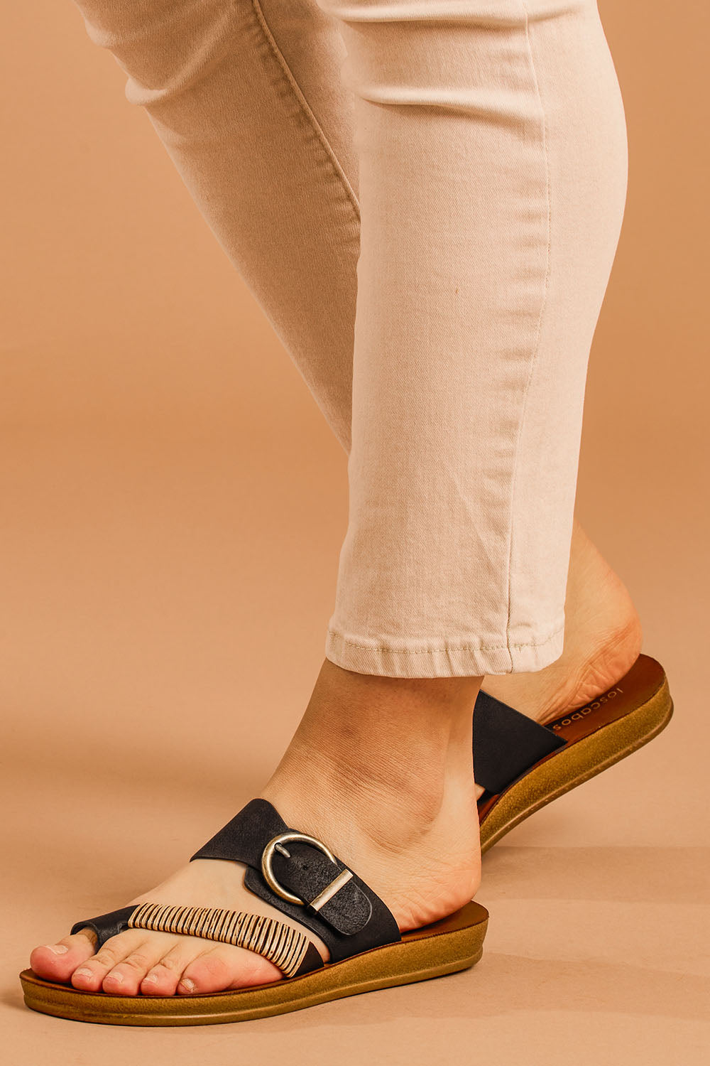 A model wearing size 38 of the Bria Flat Sandal in colour Black (Black), from the front, cropped image