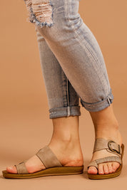 A model wearing size 38 of the Bria Flat Sandal in colour Taupe, from the front, cropped image