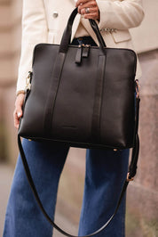 A model wearing the Rhodes Laptop Bag in colour Black (Black), from the front, showing the whole outfit