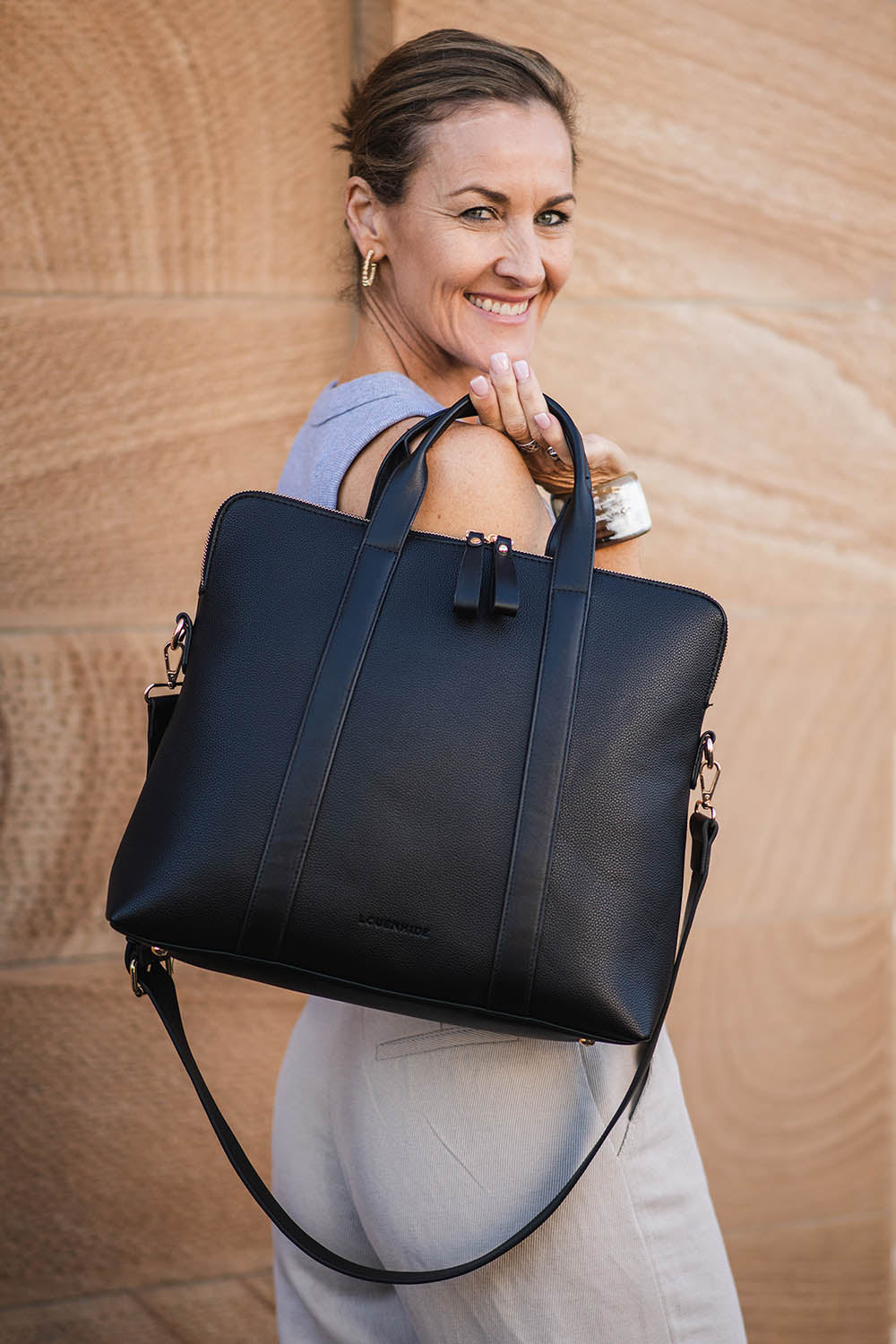 A model wearing the Rhodes Laptop Bag in colour Black (Black), from the front, showing the whole outfit