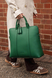 A model wearing the Rhodes Laptop Bag in colour Green (Green), from the front, showing the whole outfit