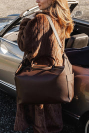A model wearing the Ohio Overnight Bag in colour Chocolate, from the front, showing the whole outfit