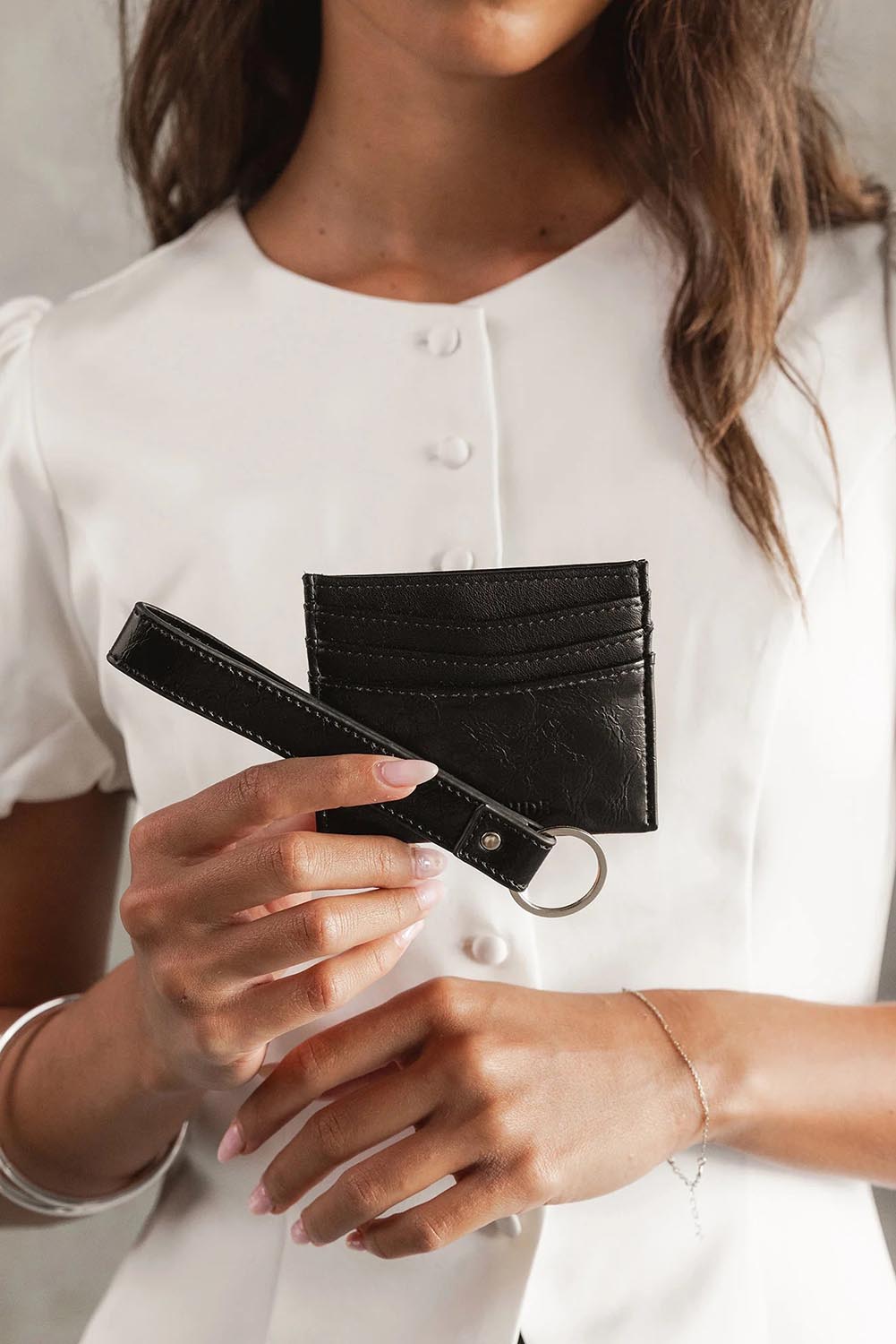 A model wearing the Ada Cardholder And Keyring in colour Blackpaten (Black), from the front, showing the whole outfit