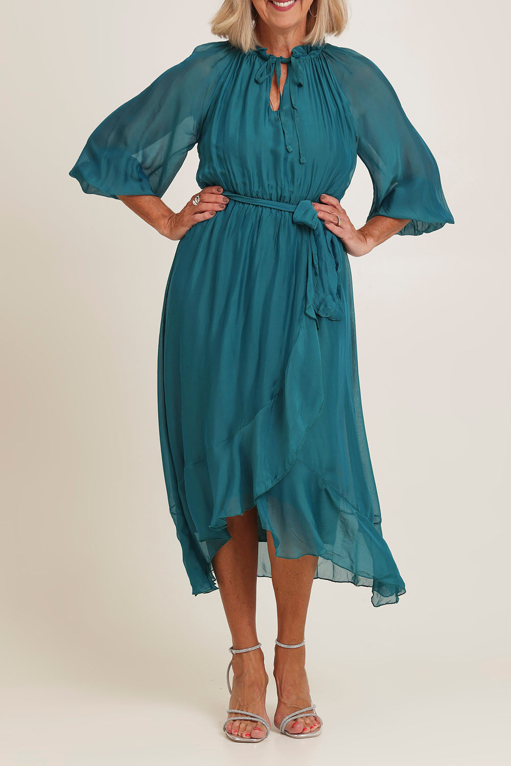 Model Sandy wearing the Long Sleeve Silk Frill Tied Neck Knee Length Dress in colour Teal (Green), from the front, cropped image