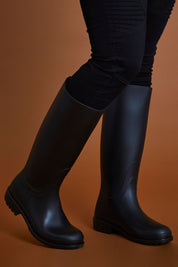 A model wearing size 40 of the Otoki Waterboot Calf Rainboot in colour Black (Black), from the front, cropped image