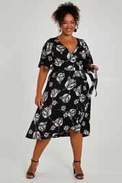 Model Alexis wearing size 16 of the Alanah Wrap Dress in colour Tulips (Black), from the front, showing the whole outfit