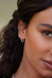A model wearing the Chia Silver Hoop Earrings in colour Silver (Metallics), from the front, cropped image