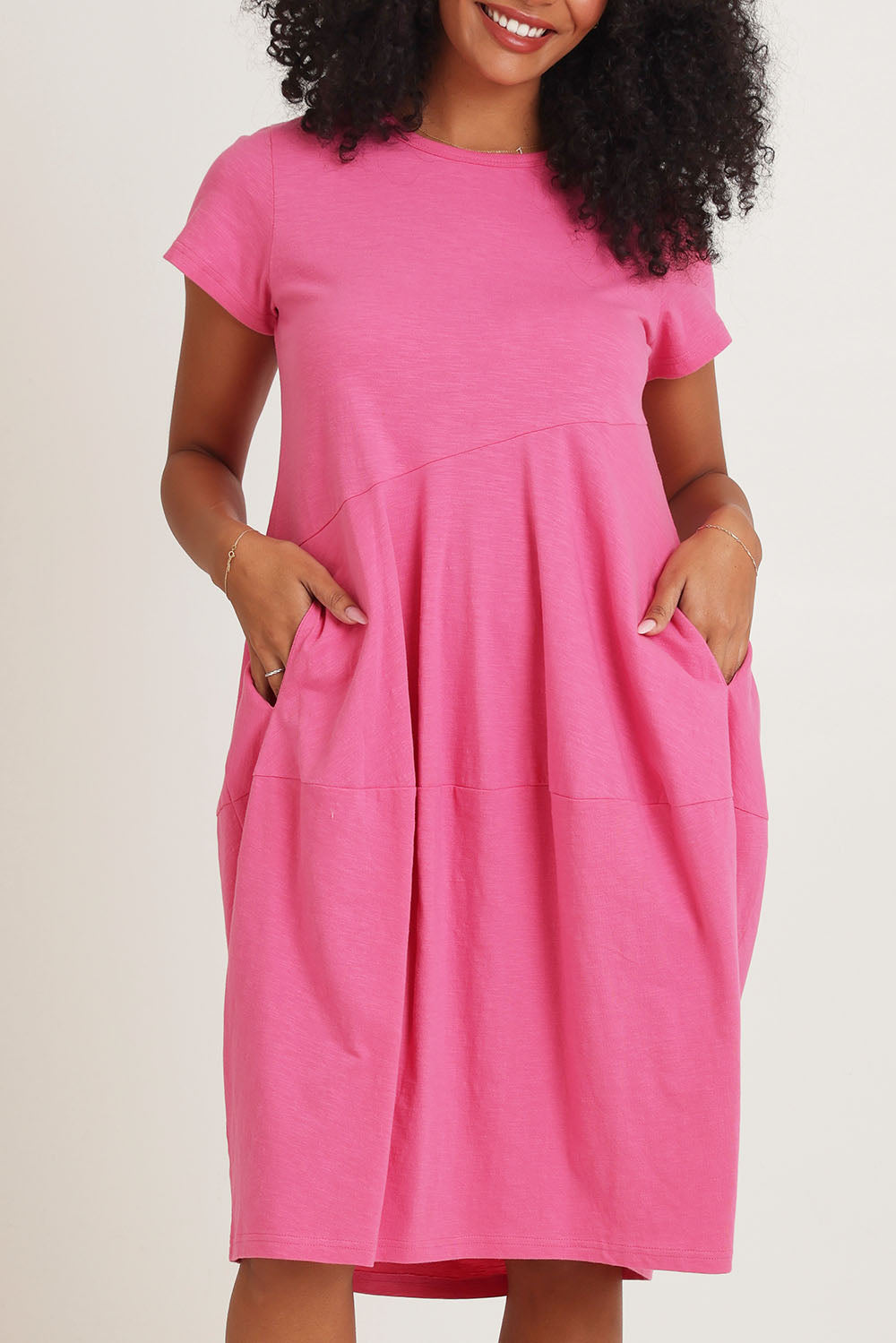 Model Ziara wearing size 10 of the Essentials Organic Cotton Bubble Dress in colour Pink (Pink), from the front, cropped image
