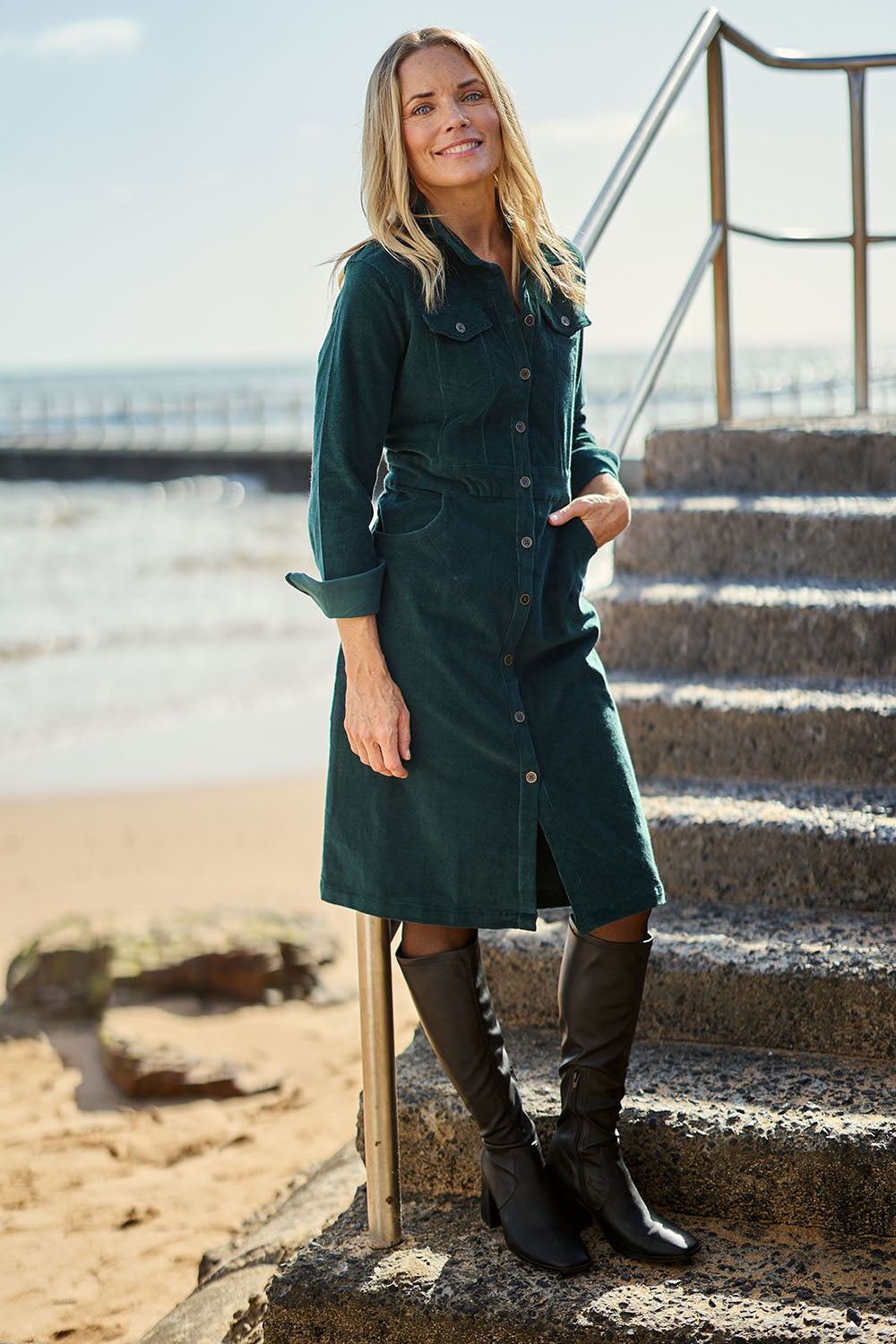 Model Maggie wearing size 10 of the Cotton Corduroy Button Dress in colour Pine (Green), from the front, showing the whole outfit
