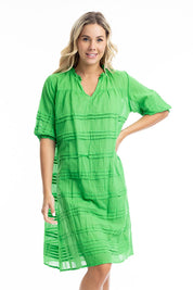 A model wearing the Essentials Organic Cotton Gauze Pleated  Dress in colour Parakeet (Green), from the front, cropped image