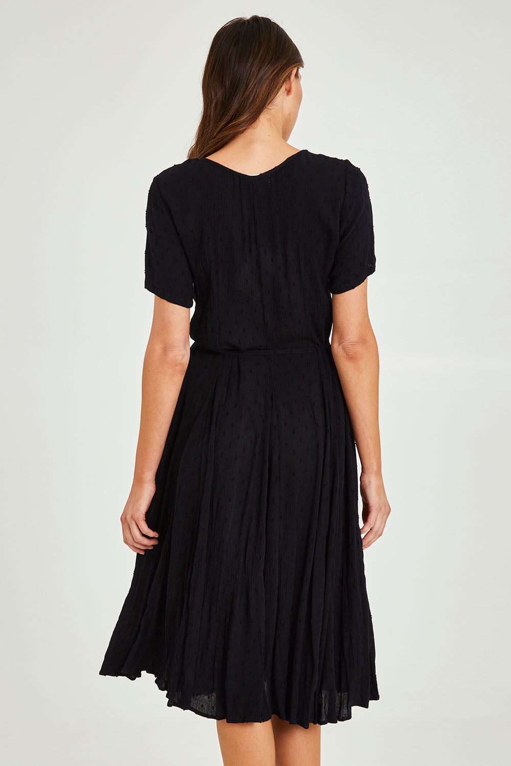 Model Madeline wearing size 10 of the Essentials Godet Short Sleeve Dress in colour Black (Black), from the back