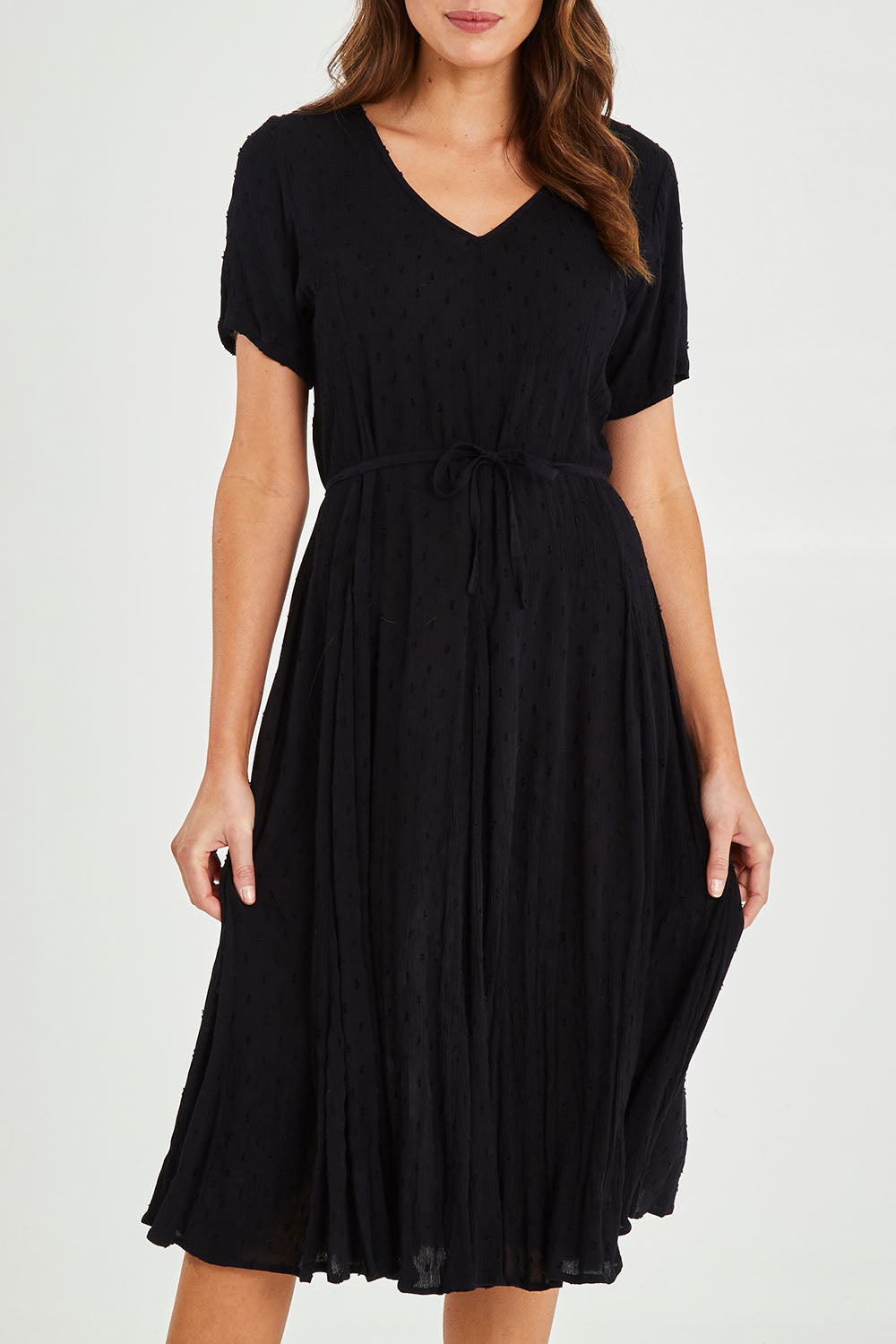 Model Madeline wearing size 10 of the Essentials Godet Short Sleeve Dress in colour Black (Black), from the front, cropped image