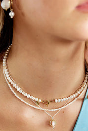 A model wearing the Pearl Fob Necklace in colour Pearl (White), from the front, cropped image