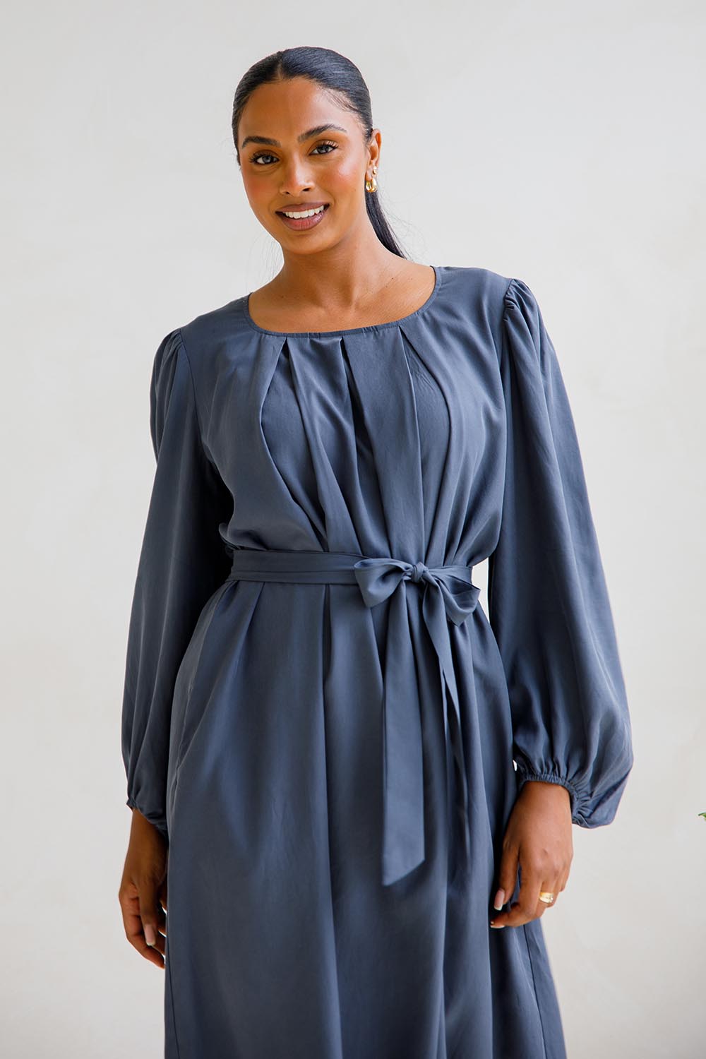 A model wearing the Jade Tencel Dress in colour Storm (Blue), from the front, cropped image