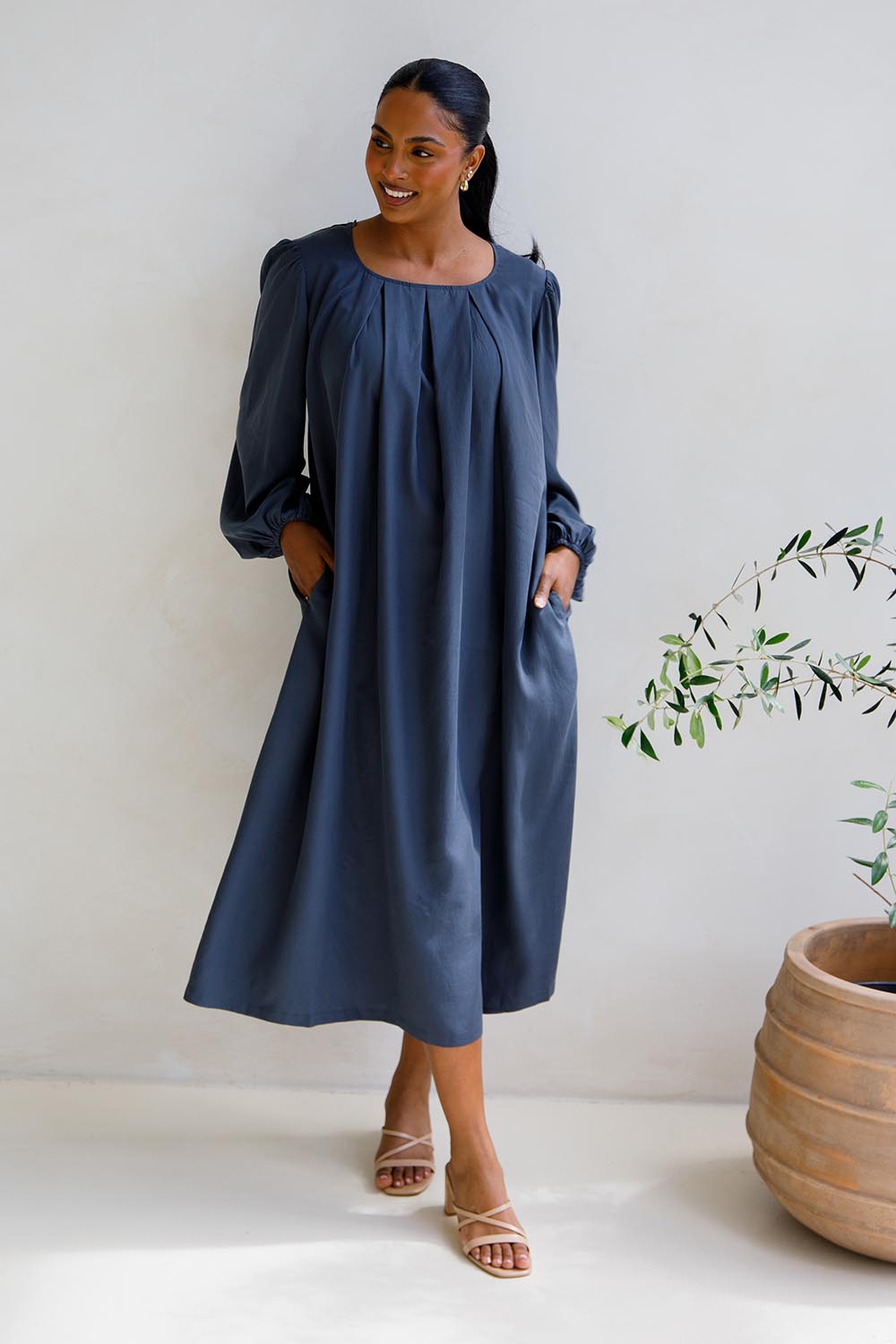 A model wearing the Jade Tencel Dress in colour Storm (Blue), from the front, showing the whole outfit