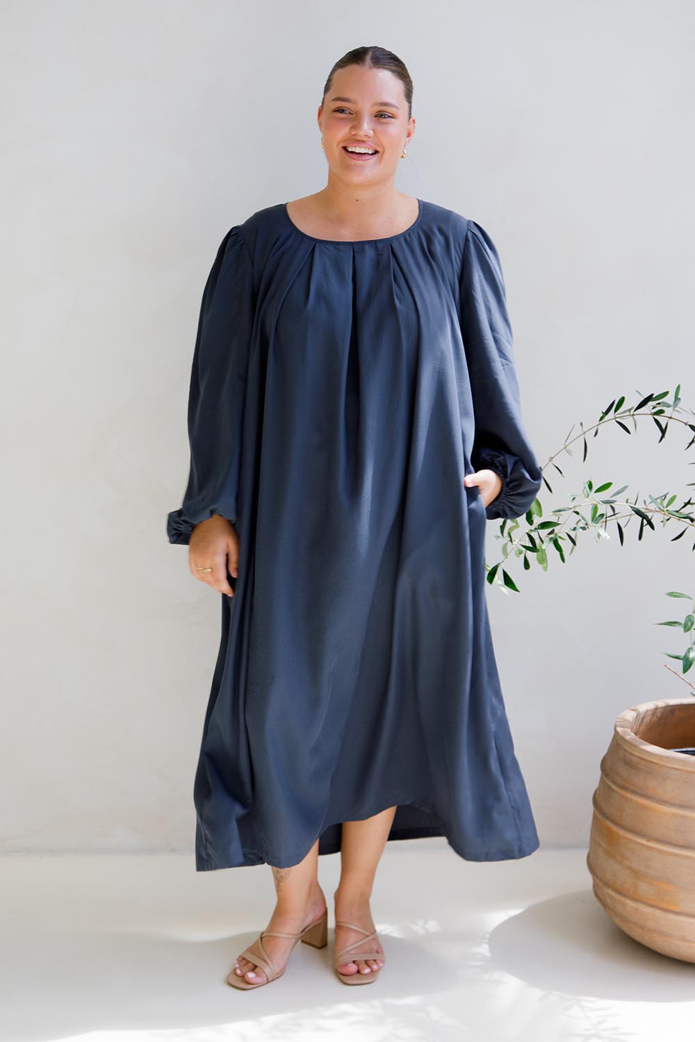 A model wearing the Jade Tencel Dress in colour Storm (Blue), from the front, showing the whole outfit
