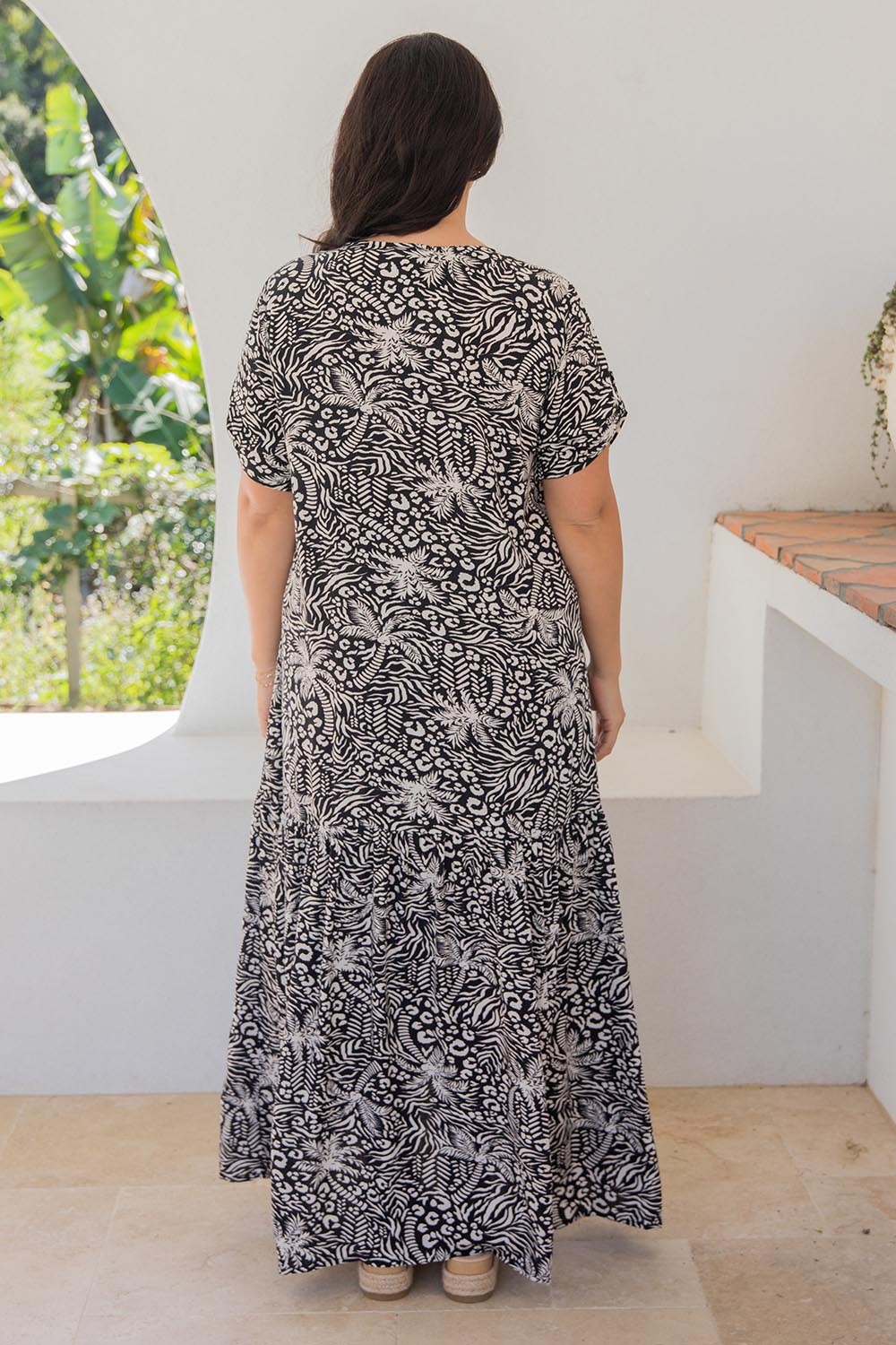 A model wearing the Peak Maxi Dress in colour Blkpalm (Black), from the back