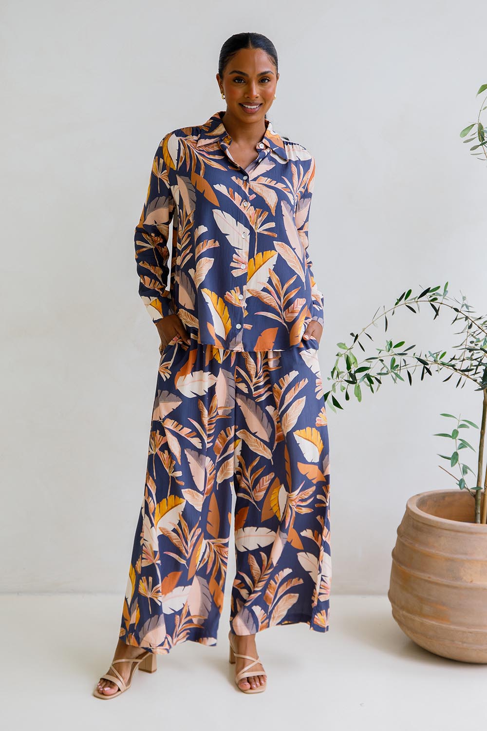 A model wearing the Aspen Pants in colour Darkpalme, from the front, showing the whole outfit