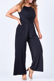 Model Laura wearing size 12 of The Cross Waist Jumpsuit in colour Black (Black), from the front, cropped image