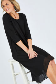 Model Chelsea wearing size 10 of The Chiffon Trim Dress in colour Black (Black), from the front, cropped image