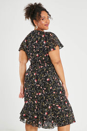 Model Alexis wearing size 16 of The Printed Chiffon Lined Dress in colour Botanical (Black), from the back