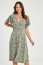 Model Madeline wearing size 10 of The Printed Jersey Faux Wrap Dress in colour Fleur (Green), from the front, cropped image