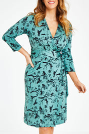 Model Laura wearing size 12 of the Belle Bird Print Wrap Dress in colour Bird (Green), from the front, cropped image