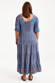 Model Monique wearing size 14 of the Paradise Found Maxi Dress in colour Denimfleur (Blue), from the back