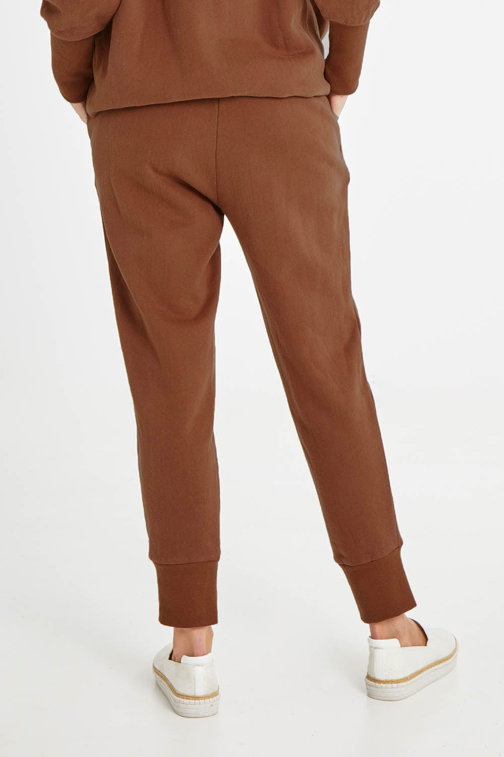 Model Madeline wearing size 10 of the Fundamentals Cosy Track Pant in colour Choc, from the back