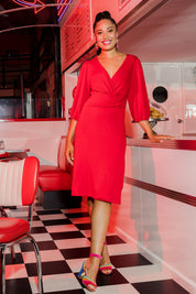 Model Olivia wearing size 10 of the Gathered Waist Faux Wrap Dress in colour Flame (Red), from the front, showing the whole outfit