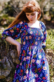 A model wearing the Raquel Shirred Dress in colour Blue (Blue), from the front, showing the whole outfit