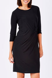 Model Perrie wearing size 10 of the Side Cross Dress in colour Black (Black), from the front, cropped image