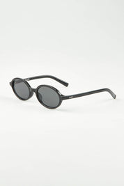 A model wearing The Bessette Sunglasses in colour Black (Black), from the front, showing the whole outfit