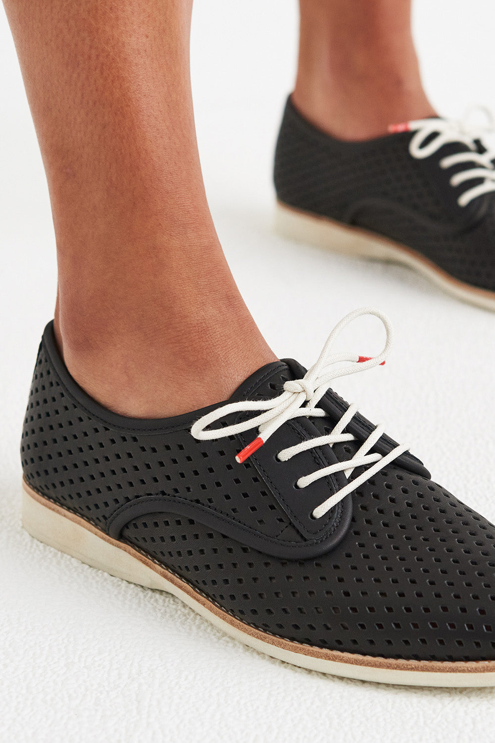 A model wearing the Derby Punch Flat in colour Black (Black), from the front, cropped image