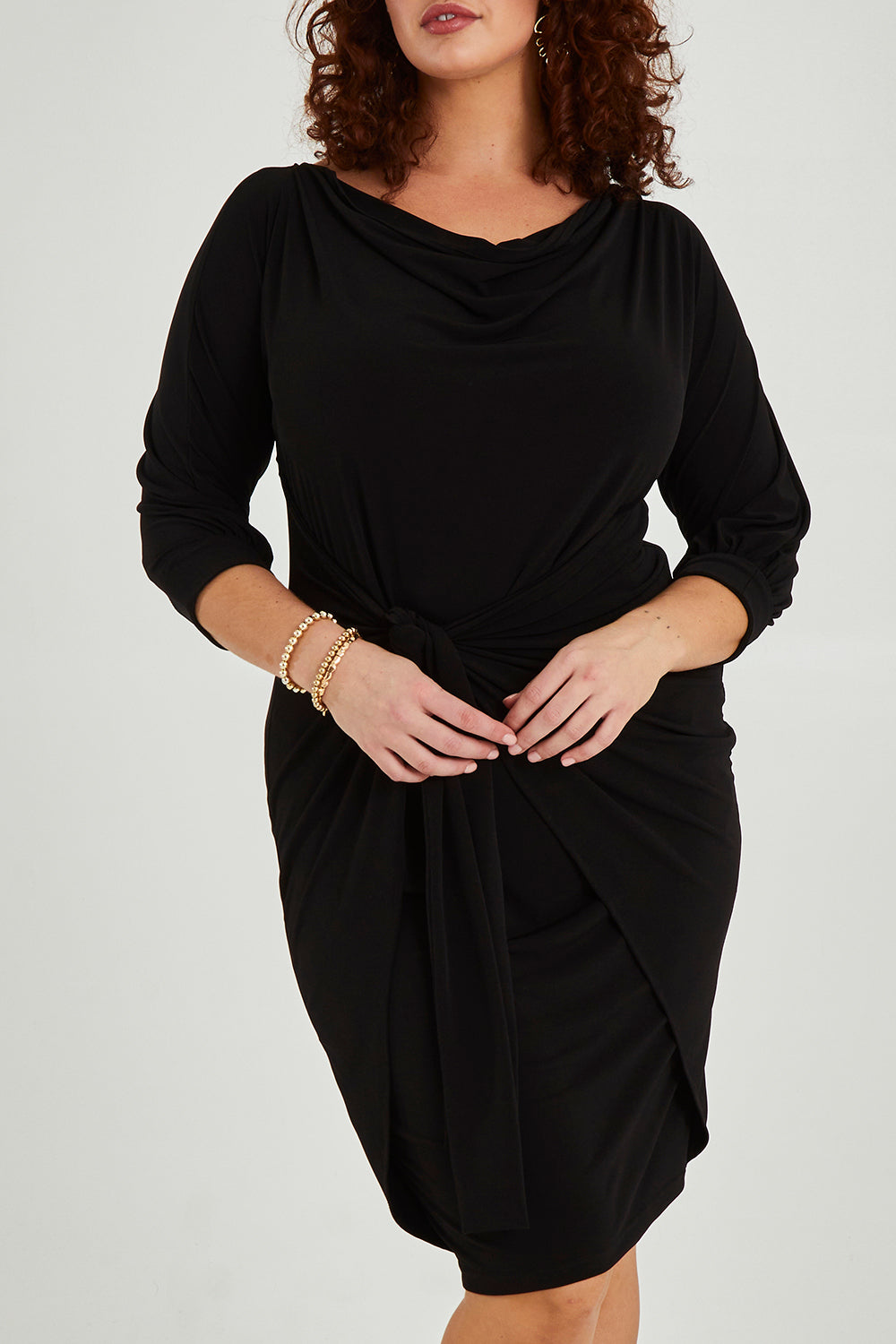 Model Maddy wearing size 16 of the Cowl Tie Drape Dress in colour Black (Black), from the front, cropped image